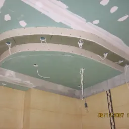 Sufit podwieszany z płyt gipsowo-kartonowych w kształcie łuku, z przygotowanymi otworami na oświetlenie punktowe i wystającymi przewodami elektrycznymi, w trakcie prac wykończeniowych.